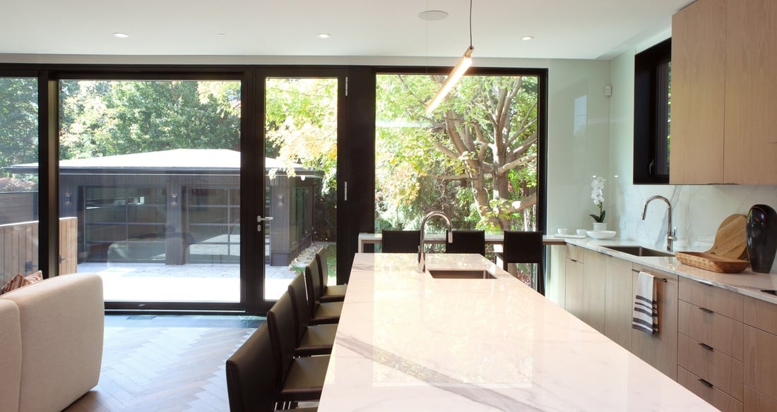 View of kitchen island with floor-to-ceiling windows in back in luxury custom home by SevernWoods Fine Homes