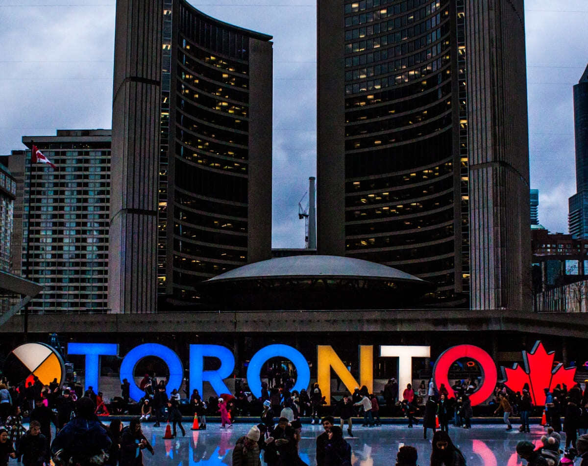 Toronto sign in front of buildings downtown at dusk with people outside